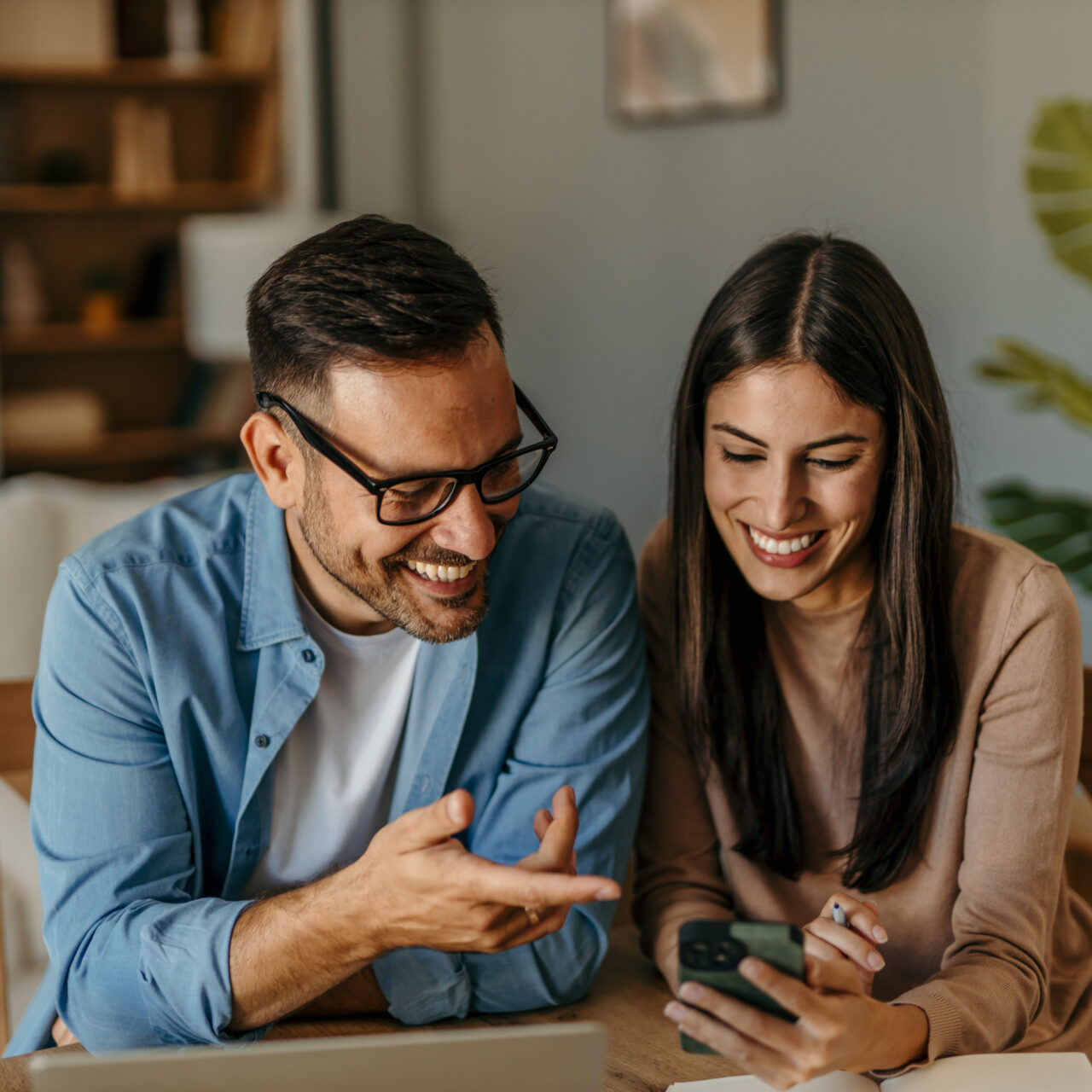 A couple in love is sitting together at a table, using a laptop and a payment card, while both are looking at insurance products on the screen